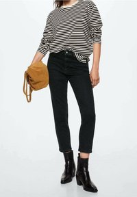 Raidallinen pitkähihaisella paidalla mustavalkoisena, yhdistettynä korkeavyötäröisiin mustiin farkkuihin ja mustiin nilkkureihin; käsissään ruskea mokkabag.