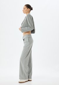 Blazer gris corto con mangas largas y pantalones de pierna ancha gris claro, ambos con un sutil patrón de cuadros. Los zapatos son blancos con acentos en beige.