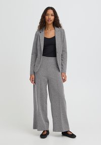 Sort-hvid stribet jakkesæt med en skræddersyet blazer og bukser med vide ben. Blødt stof med en tekstureret sildebensmønster. Bruges over en sort top.