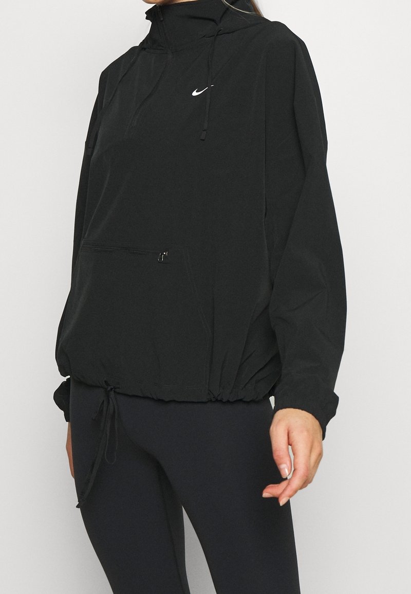 Sort Nike pullover jakke med høj krave, lynlås foran lomme, snoretræk i hæm og reflekslogo. Letvægtsstof med en glat tekstur.