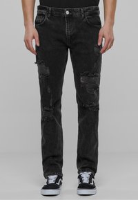 Musta kulunut farkut, joissa näkyviä repeämiä, slim-fit muotoilu, viisi-taskumalli ja hopeinen nappikiinnitys. Yhdistetty mustiin lenkkareihin.