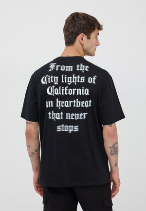 T-shirt di cotone nero con maniche corte, con testo bianco sul retro che recita: "Dalle luci della città della California in un battito che non si ferma mai."