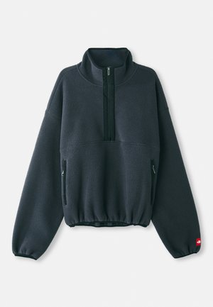 Pullover in pile grigio scuro con colletto alto, chiusura frontale a metà zip, orlo elasticizzato e tasche laterali con zip. Presenta una superficie testurizzata.