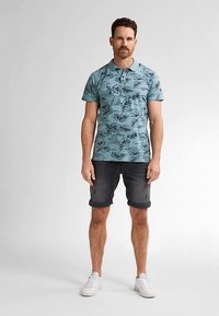 Krátký rukáv polotriko v tyrkysové barvě s tmavým květinovým potiskem, kombinované s tmavými džínovými kraťasy. Outfit doplňují bílé tenisky.