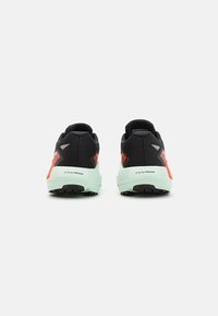 Baskets de running en mesh noir avec des accents réfléchissants, dotées d'une semelle intermédiaire en mousse verte et d'une semelle extérieure en caoutchouc noir à motif.