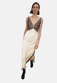 Robe de nuit en crème avec des bordures en dentelle, présentant un décolleté en V profond, mettant en valeur des accents en dentelle noire le long du corsage et une fente latérale haute.