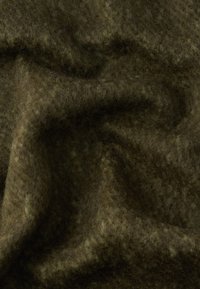 Σκούρο πράσινο υφασμάτινο με υφή και απαλή, αφράτη επιφάνεια, που περιλαμβάνει ένα μείγμα ανοιχτότερων και σκουρότερων ινών δημιουργώντας ένα διακριτικό σχέδιο.