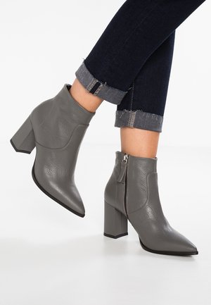 Szare skórzane botki ankle z ostro zakończonym noskiem, blokowym obcasem i zamkiem błyskawicznym po boku. Materiał ma teksturowane wykończenie, a design charakteryzuje się elegancką sylwetką.