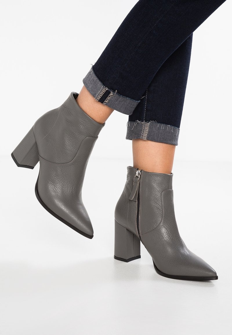 Bottines en cuir gris avec un bout pointu, un talon bloc et une fermeture éclair sur le côté. Le matériau a une finition texturée et le design présente une silhouette élégante.
