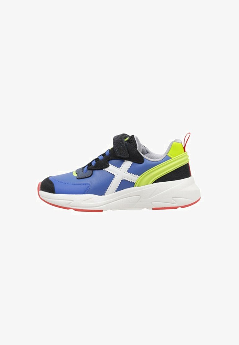 Zapatilla deportiva azul con acentos blancos, detalle lateral verde, talón negro, tejido texturizado y suela roja. Incluye cordones y una correa de velcro.