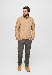 Beige fleece jacket with high collar, front zipper, and side pockets. Paired with olive cargo pants and tan boots.