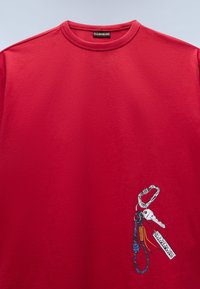 Κόκκινο φούτερ με λαιμόκοψη crewneck, με γραφικό μπρελόκ που απεικονίζει ένα καραμπίνερ, λευκό κλειδί και την ετικέτα "Napapijri" στο κάτω δεξί μέρος μπροστά.