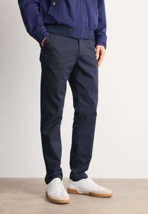 Pantalones de algodón azul marino con un diseño de pierna recta. Textura suave y ajuste moderno, combinados con zapatillas blancas con acentos beige.