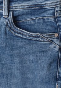 Gros plan d'une poche de jean en denim bleu avec des coutures visibles, une boucle de ceinture et un rivet en métal.