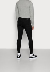 Jeans negros ajustados con bolsillos traseros, combinados con una camiseta de manga larga gris claro y zapatillas negras y blancas.
