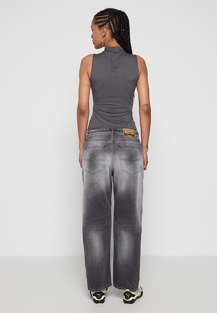Top grigio senza maniche con arricciature, abbinato a jeans larghi sbiancati di un grigio chiaro. Distintivo patch con logo sulla vita, indossato con sneakers spesse.