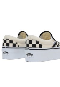 Zapatillas slip-on en un diseño de tablero de ajedrez en blanco y negro con una suela blanca gruesa y el logo de Vans en el talón. Material de lona con una textura suave.