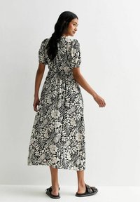 Vestido maxi con estampado floral en blanco y negro, mangas cortas abullonadas, cintura ceñida y falda fluida, combinado con sandalias negras.