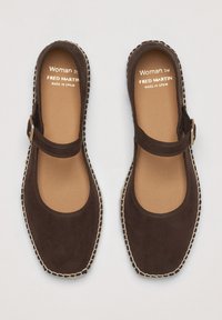 Scarpe Mary Jane in suede marrone con cinturino, caratterizzate da una punta arrotondata, cuciture beige e un logo inciso. Suola piatta.