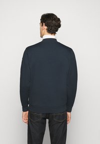 Felpa blu navy scuro con collo rotondo e polsini a costine. Materiale in cotone liscio, design minimalista, senza motivi o dettagli visibili.