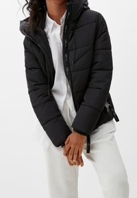 Czarna kurtka puchowa z zamkiem z przodu, kapturem i elastycznymi mankietami. Posiada pikowany wzór oraz akcenty logo na suwakach.