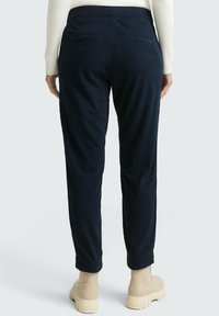 Granatowe spodnie sztruksowe o fakturowanej powierzchni, z elastycznym pasem i dwoma tylnymi kieszeniami, zestawione z beżowymi botkami za kostkę.