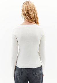 Långärmad, vit topp med rundad halsringning, mjuk textur, tight passform och något böjd nederkant, matchad med mörka denimjeans.