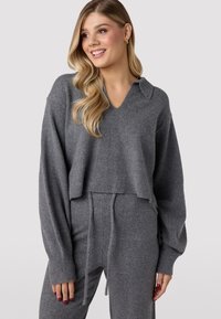 Pullover grigio corto in morbido filato con scollo a V e colletto. Maniche lunghe, leggermente voluminose, con polsini a costine, abbinato a pantaloni con cordoncino.