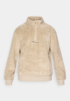 Beige fleecetrui met een ritskraag, gemaakt van een zachte, gestructureerde stof en voorzien van een klein geborduurd logo op de borst.