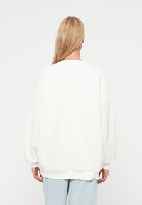 Felpa bianca oversize in tessuto morbido e strutturato con scollo rotondo, polsini e orlo a coste; vestibilità comoda. Vista dal retro.