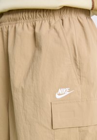 Bež Nike cargo kratke hlače z elastičnim pasom, stranskimi žepi in žepom z zatičem. Na sprednji strani je bele barve izvezen logotip.