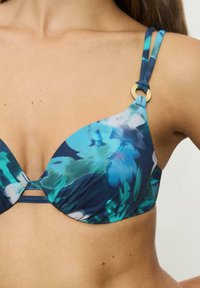 Biustonosz bikini w kwiatowy wzór w niebieskich, zielonych i białych kolorach; posiada V-kształtną miseczkę, cienkie ramiączka oraz detal w postaci złotego pierścienia.