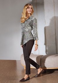 Hemdbluse mit geometrischem und Tiermuster in Schwarz, Creme und Burgunderrot; kombiniert mit schmalen schwarzen Hosen und dunklen Slippern.