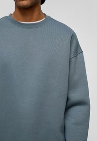 Lichtblauwe sweatshirt met een geribbelde kraag en verlaagde schouders. De stof is zacht en glad, met een eenvoudige uitstraling zonder patronen.