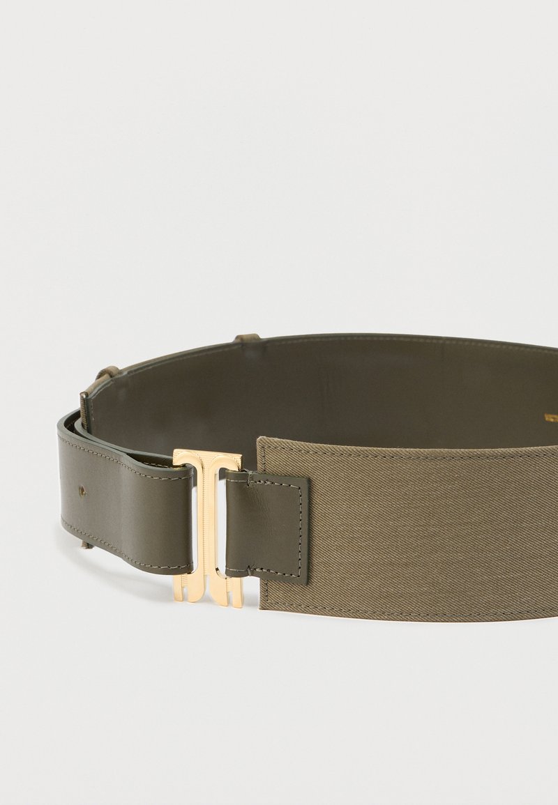 Ceinture verte avec un design en cuir lisse et tissu texturé. Elle présente une boucle brillante dorée et une forme plate et large.