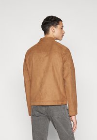 Veste en suede marron avec une texture lisse, un col et une coupe droite. Présente des coutures minimales et un design épuré.