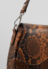 Sac à main en cuir à motif serpent brun et noir avec un rabat incurvé, une fermeture en métal argenté et une surface texturée. Il est doté d'une bandoulière robuste.