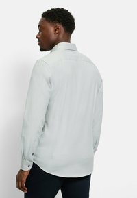 Hellgraues Langarmhemd mit subtiler Textur, spitzem Kragen und geknöpften Manschetten. Das Hemd hat einen abgerundeten Saum und eine figurnahe Passform.