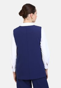 Marineblaues ärmelloses Weste-Rücken-Design, texturierten Stoff, klare Linien, ergänzt durch ein weißes Hemd mit Kragen und Knopfdetails an den Ärmeln.