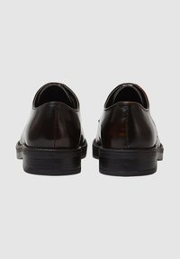Scarpe in pelle marrone con una finitura liscia, punta tonda e suola nera bassa, viste da dietro, che evidenziano i dettagli della cucitura.
