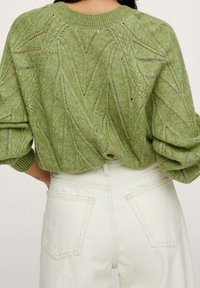 Grüner gestrickter Pullover mit einem strukturierten Blättermuster, runder Halslinie und Puffärmeln. Kombiniert mit hochgeschnittenen weißen Hosen.