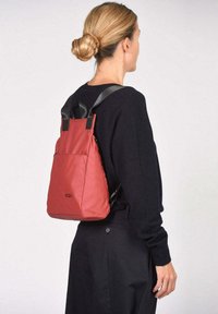 Rode nylon rugzak met zwarte banden, met een minimalistisch ontwerp en een buitentas. Lichtgewicht, met een zachte textuur en een gestroomlijnde vorm.