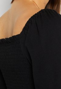 Top nero con dettagli arricciati attorno alle spalle. Tessuto morbido, texture arricciata e design off-the-shoulder nel collo.
