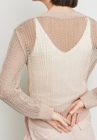 Leichter, gestrickter Pullover mit V-Rücken-Design. Die Farben reichen von Creme bis zartem Rosa mit gerippten Bündchen und einem strukturierten Muster.