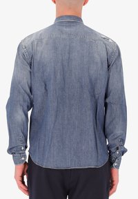 Camicia di jeans azzurra con maniche lunghe, polsini a bottone, colletto classico e un dettaglio leggermente usurato sulla spalla.