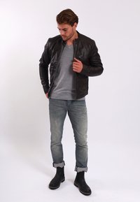 Chaqueta de cuero marrón con un diseño ajustado, camiseta de manga larga gris, jeans claros desgastados y botas negras hasta el tobillo.
