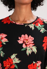 Vestido negro con estampado floral que presenta grandes flores rojas y rosas con hojas verdes, escote redondo y una textura de tela suave.