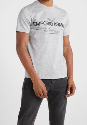 T-shirt grigia a maniche corte in cotone, con una stampa grafica nera che riporta il testo "EMPORIO ARMANI" attraversando il petto.
