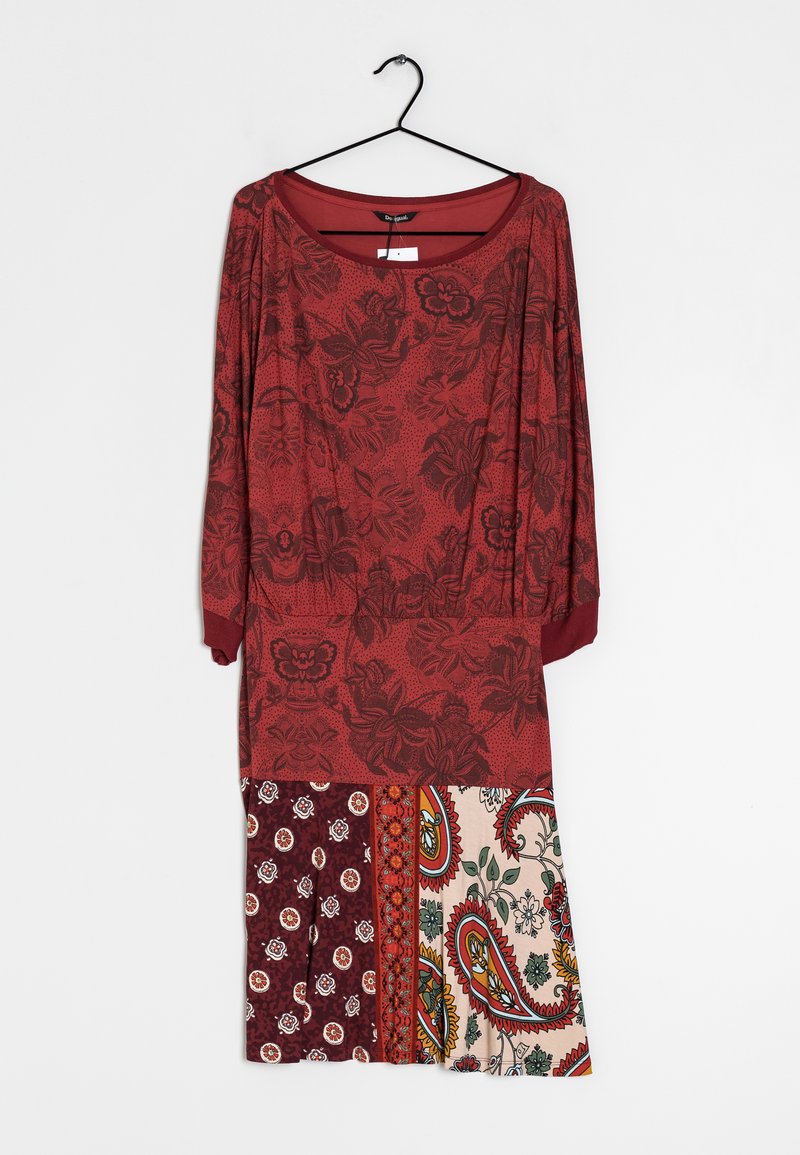 Robe rouge avec des motifs floraux en haut et une jupe en patchwork présentant des designs paisley et circulaires. Manches longues et décolleté rond.