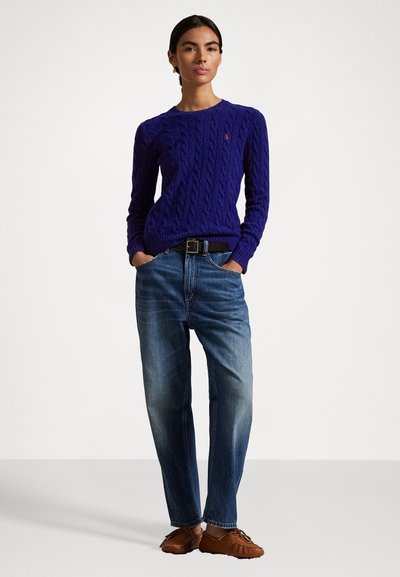 Suéter roxo de malha canelada com mangas longas, decote redondo, combinado com jeans azul claro e sapatos estilo mocassim castanhos.